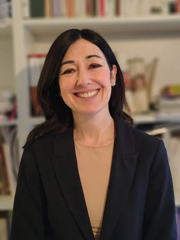 Immagine di archivio di una donna sorridente in un ambiente interno, con scaffali di libri sullo sfondo.