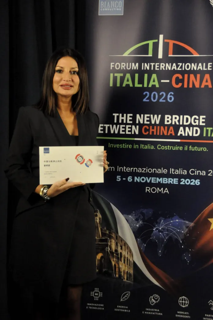 Una donna in abito nero tiene un documento davanti a un pannello promozionale del Forum Internazionale Italia–Cina 2026.