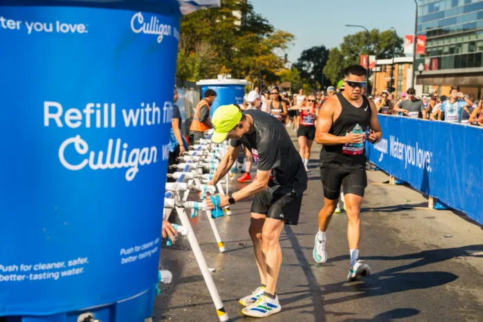 Una persona riempie una borraccia a una stazione Culligan mentre altri runner passano accanto ai punti di rifornimento.