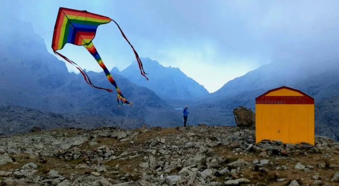 Paesaggio montano con aquilone colorato e piccolo rifugio arancione, immagine rappresentativa della Valle Varaita.