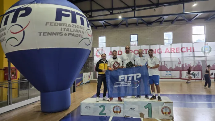 Cinque persone posano sul podio con una bandiera FITP; sullo sfondo si vedono un campo sportivo e un grande gonfiabile FITP.