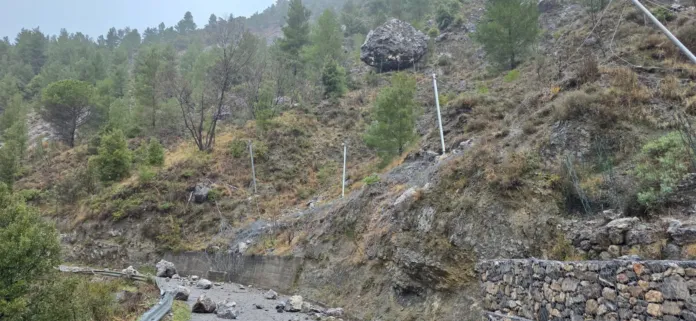 Foto di archivio di una strada con barriere danneggiate in un'area collinare rocciosa.