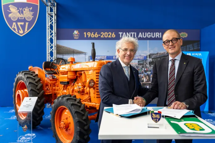 Trattore agricolo arancione esposto; accanto, due persone sono sedute a un tavolo con documenti.