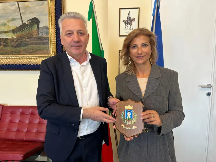 Fotografia di archivio o illustrativa di un incontro istituzionale tra due persone che si stringono la mano, con bandiere e dipinto sullo sfondo.