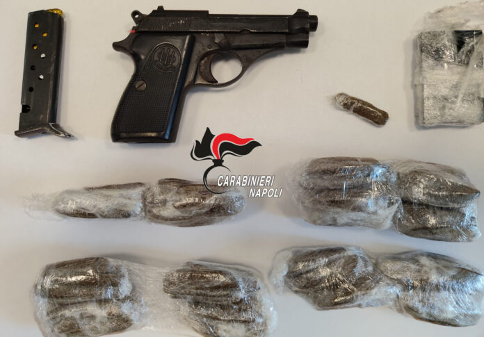 Pistola Beretta con caricatore e involucri di stupefacente avvolti in plastica trasparente su una superficie bianca, con logo Carabinieri Napoli al centro dell'immagine.
