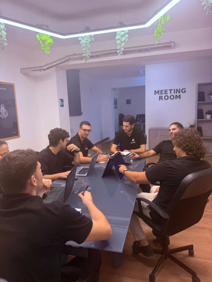 Un gruppo di persone è seduto attorno a un tavolo con computer portatili in una sala riunioni.