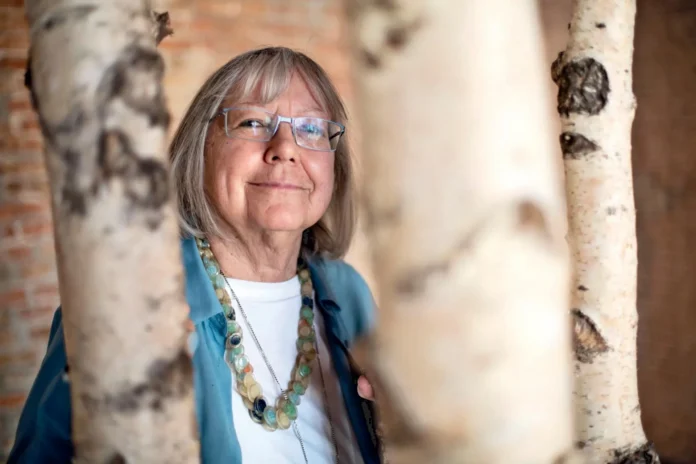 Ritratto di Vivian Lamarque con occhiali e collana colorata tra tronchi di alberi