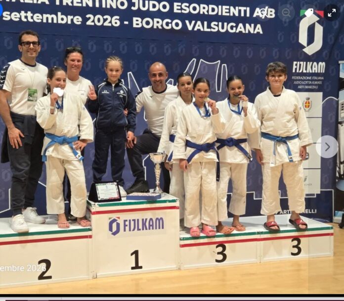 Gruppo di giovani judoka con medaglie e trofei sul podio durante una competizione di judo.