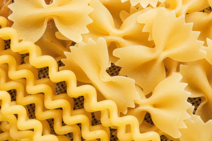 Primo piano di pasta secca di diversi formati, tra cui farfalle e pasta ondulata.