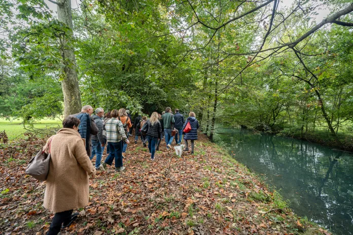 Persone in passeggiata lungo un sentiero naturale vicino a un fiume in un'area verde con alberi