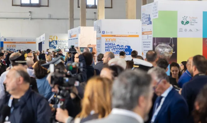 Persone si muovono tra stand espositivi con pannelli della Borsa Mediterranea del Turismo Archeologico.