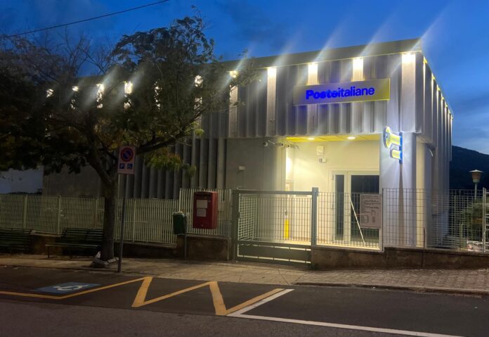 Edificio con insegna Poste Italiane, ripreso di sera dietro una recinzione.