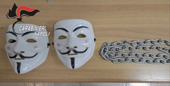 Due maschere di Guy Fawkes e una catena poste su un tavolo, immagine relativa a un intervento dei Carabinieri a Napoli.