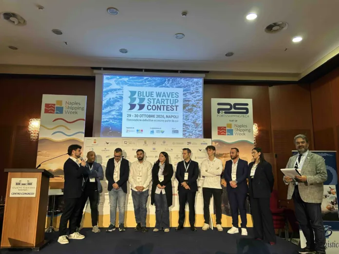 Un gruppo di persone è in piedi su un palco; alle loro spalle, uno schermo mostra la scritta Blue Waves Startup Contest.