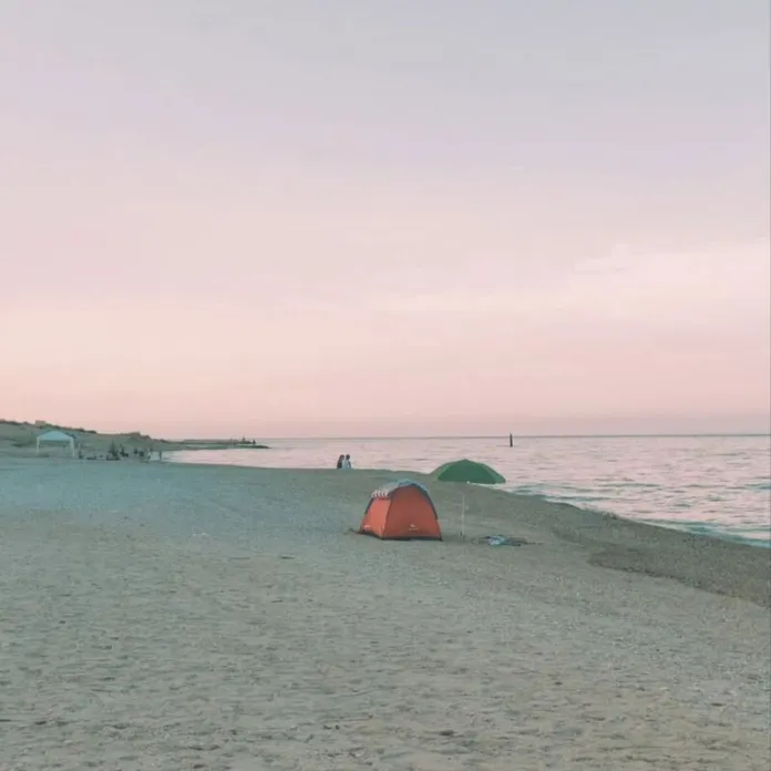 Una tenda arancione sulla spiaggia, vicino al mare, sotto un cielo rosato.