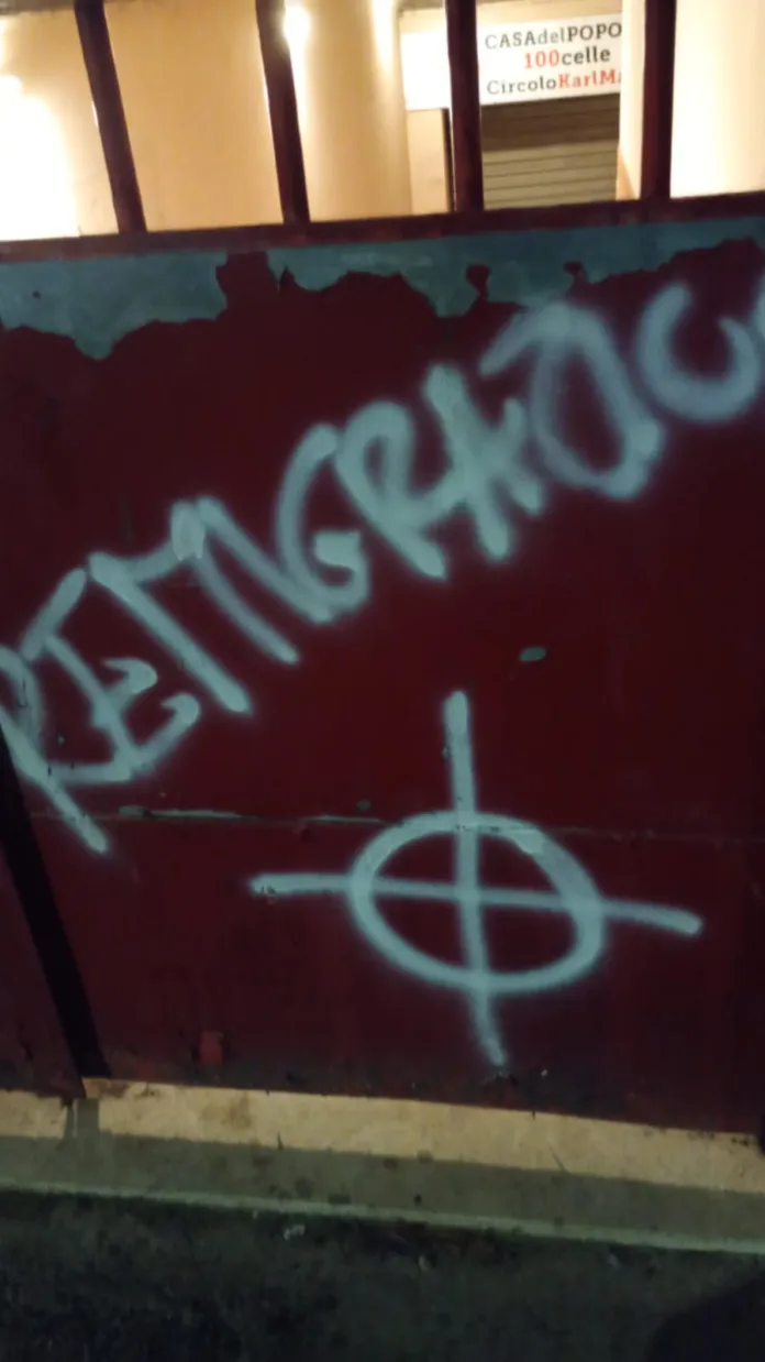 Primo piano di un cancello rosso con scritte e un simbolo realizzati con vernice chiara.