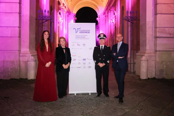 Quattro persone davanti a un pannello della Fondazione Umberto Veronesi, sotto un arco illuminato di rosa.