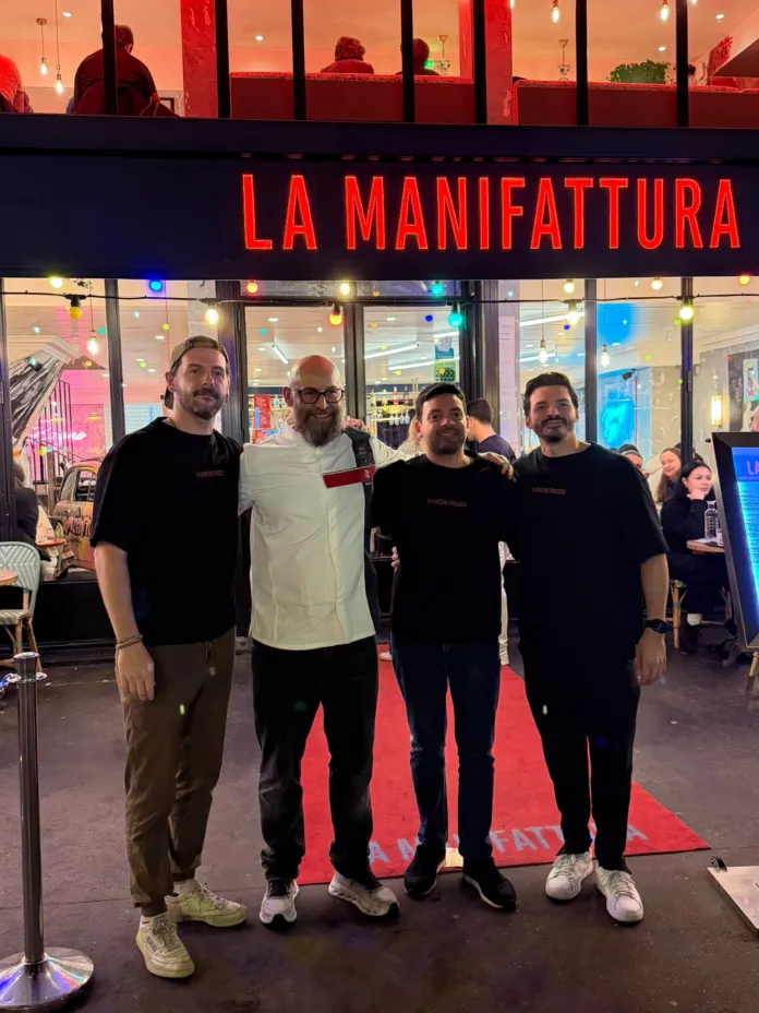 Quattro persone posano davanti all’ingresso illuminato della pizzeria La Manifattura.